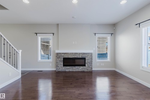 Living area featuring a stone-clad fireplace with an integrated electric insert, dark wood-finish flooring, recessed ceiling lighting, and multiple windows with white blinds - 611 176 Street, Edmonton, AB - Indoor Photo Showing Living Room With Fireplace