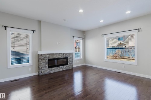 Spacious room featuring rich wood-finish flooring and a stone-clad fireplace with a dark-framed insert - 611 176 Street, Edmonton, AB - Indoor Photo Showing Living Room With Fireplace