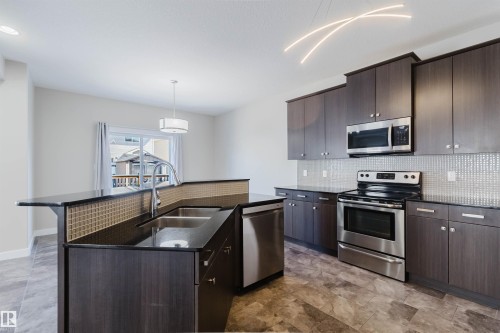 Modern kitchen featuring dark wood-finish cabinetry, stainless steel appliances, dark countertops, and a mosaic tile backsplash - 611 176 Street, Edmonton, AB - Indoor Photo Showing Kitchen With Double Sink With Upgraded Kitchen