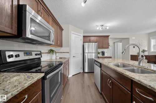 The kitchen features stainless steel appliances, granite countertops, wood cabinetry, and a double basin sink - 2118 52A Street, Edmonton, AB - Indoor Photo Showing Kitchen With Double Sink