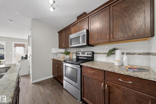 This kitchen features rich wood cabinetry, stainless steel appliances including a microwave and range, and light-colored granite countertops - 2118 52A Street, Edmonton, AB - Indoor Photo Showing Kitchen
