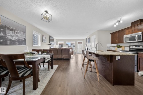 Open concept living area featuring hardwood floors, a kitchen island with seating, dark wood cabinetry, and stainless steel appliances - 2118 52A Street, Edmonton, AB - Indoor