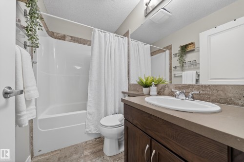 The bathroom features a vanity with a countertop and an integrated sink, a mirror, and a bathtub with a shower and a shower curtain - 2118 52A Street, Edmonton, AB - Indoor Photo Showing Bathroom