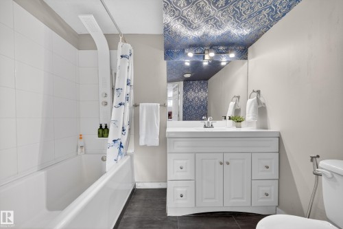 The bathroom features a white vanity with a rectangular sink, a white bathtub with white subway tile surround, and a ceiling with patterned wallpaper - 2118 52A Street, Edmonton, AB - Indoor Photo Showing Bathroom