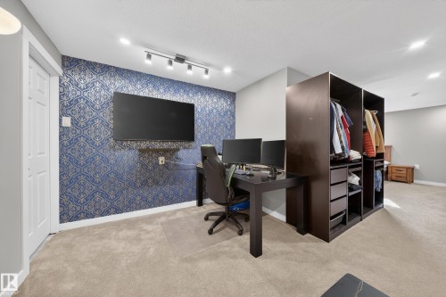 This versatile space features carpeting, a striking blue and gold patterned accent wall, and recessed lighting - 2118 52A Street, Edmonton, AB - Indoor