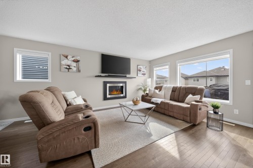 The living room features hardwood flooring, an electric fireplace, and large windows providing ample natural light - 2118 52A Street, Edmonton, AB - Indoor Photo Showing Living Room With Fireplace