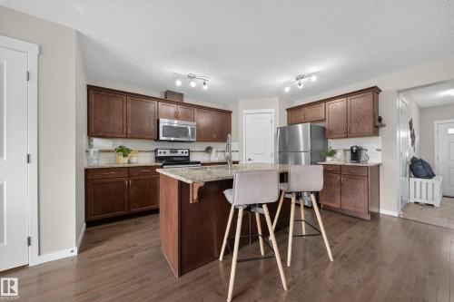 The kitchen features dark wood cabinetry, stainless steel appliances, and a central island with a granite countertop - 2118 52A Street, Edmonton, AB - Indoor Photo Showing Kitchen