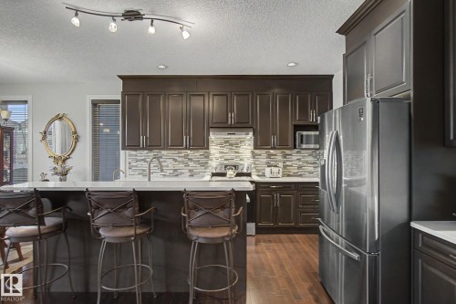 Kitchen featuring dark wood-finish cabinetry, a multi-tone tile backsplash, and stainless steel appliances - 805 Hodgins Road, Edmonton, AB - Indoor Photo Showing Kitchen With Stainless Steel Kitchen With Upgraded Kitchen