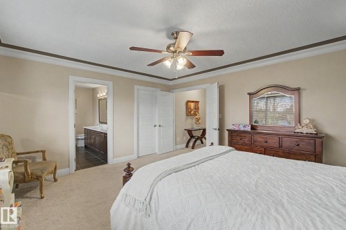 Carpeted bedroom featuring a ceiling fan with integrated lighting, crown molding, and a visible doorway leading to a bathroom with a dark wood-finish vanity and tiled flooring - 805 Hodgins Road, Edmonton, AB - Indoor Photo Showing Bedroom