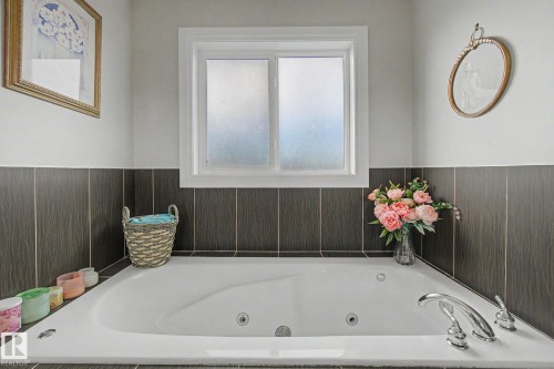 Soaking tub featuring chrome fixtures, dark vertical tile wainscoting, and a privacy window - 805 Hodgins Road, Edmonton, AB - Indoor
