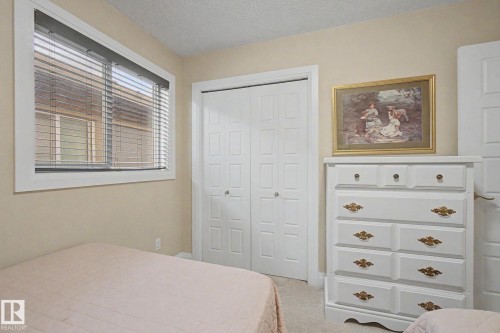 Neutral-toned bedroom featuring a window with horizontal blinds, bi-fold closet doors, and light-colored wall-to-wall carpeting - 805 Hodgins Road, Edmonton, AB - Indoor Photo Showing Bedroom