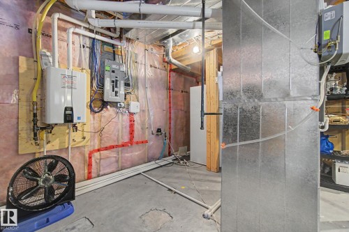 Utility room featuring a tankless water heater, electrical panel, exposed insulated walls, and concrete flooring - 805 Hodgins Road, Edmonton, AB - Indoor Photo Showing Basement