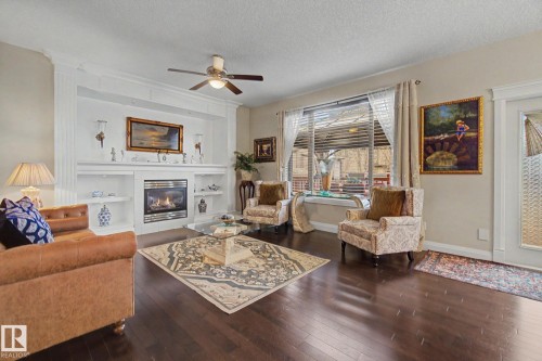 Inviting living area featuring a built-in fireplace with custom shelving, dark wood-finish flooring, a ceiling fan, and large windows with blinds - 805 Hodgins Road, Edmonton, AB - Indoor Photo Showing Living Room With Fireplace