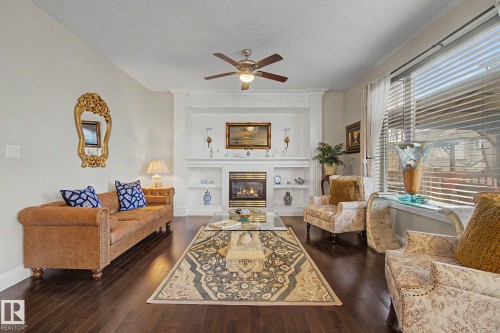 Living area featuring a prominent fireplace surround with built-in shelving, dark wood-finish flooring, a ceiling fan, and large windows with blinds - 805 Hodgins Road, Edmonton, AB - Indoor Photo Showing Living Room With Fireplace