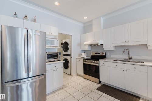 White kitchen featuring stainless steel appliances, white cabinetry, a double basin sink, and tile flooring - 19 1659 Jamha Road, Edmonton, AB - Indoor Photo Showing Kitchen With Stainless Steel Kitchen With Double Sink