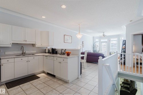Kitchen featuring white cabinetry, light-toned countertops, a stainless steel sink, and white tile flooring - 19 1659 Jamha Road, Edmonton, AB - Indoor Photo Showing Kitchen With Double Sink