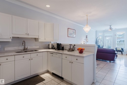 Kitchen featuring white cabinetry with brushed nickel hardware, light-toned countertop, stainless steel sink with gooseneck faucet, and white appliances - 19 1659 Jamha Road, Edmonton, AB - Indoor Photo Showing Kitchen With Double Sink