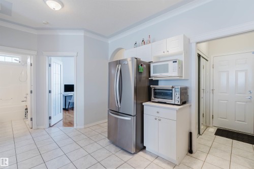 Kitchen area featuring white tile flooring, stainless steel refrigerator, white cabinetry, and an arched doorway - 19 1659 Jamha Road, Edmonton, AB - Indoor Photo Showing Kitchen