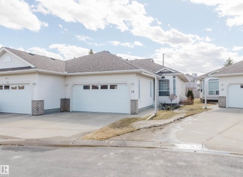 White siding exterior featuring attached garages with panel windows, bay windows, and stone veneer accents - 19 1659 Jamha Road, Edmonton, AB - Outdoor With Facade