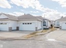 White siding exterior featuring attached garages with panel windows, bay windows, and stone veneer accents - 19 1659 Jamha Road, Edmonton, AB  - Outdoor With Facade 