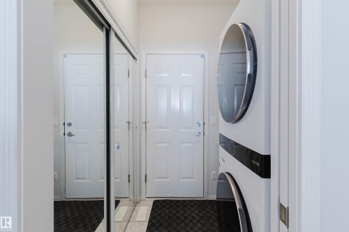 Stackable laundry appliances complement the space, featuring a mirrored sliding closet door, white paneled doors, and tiled flooring - 19 1659 Jamha Road, Edmonton, AB - Indoor Photo Showing Laundry Room