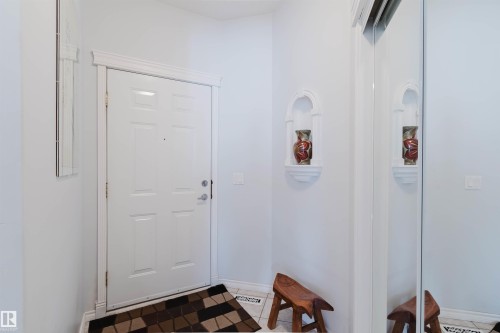 Entryway featuring a paneled door with decorative trim, a built-in wall niche, and mirror-fronted sliding closet doors - 19 1659 Jamha Road, Edmonton, AB - Indoor Photo Showing Other Room