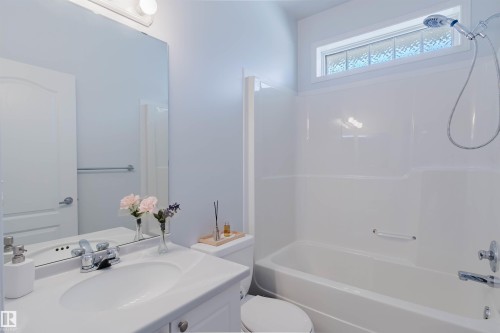 Bathroom featuring a white vanity with an integrated sink, a large wall-mounted mirror, and a full-size bathtub with an overhead shower and a transom window - 19 1659 Jamha Road, Edmonton, AB - Indoor Photo Showing Bathroom