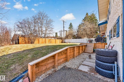 Expansive backyard featuring a tiered wooden retaining wall, a gravel and paver stone walkway, a multi-level wooden deck with steps, and a stucco exterior with blue window shutters - 1 Greenwich Crescent, St. Albert, AB - Outdoor