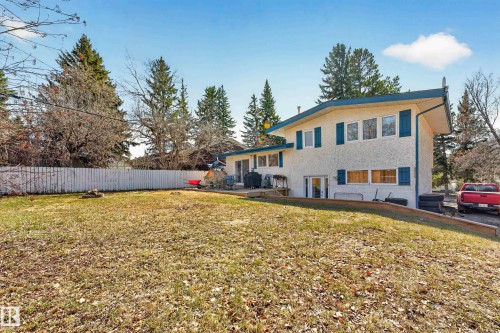 Rear exterior featuring a sloped lawn, white picket fencing, mature perimeter trees, and a ground-level patio - 1 Greenwich Crescent, St. Albert, AB - Outdoor