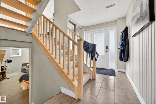 Entryway featuring natural wood staircase, slate-style tile flooring, vertical plank wall paneling, and a frosted glass-paneled front door - 1 Greenwich Crescent, St. Albert, AB - Indoor Photo Showing Other Room