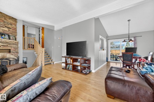 Spacious living area featuring wood-finish flooring, a stone-clad fireplace, and neutral wall tones - 1 Greenwich Crescent, St. Albert, AB - Indoor Photo Showing Living Room With Fireplace