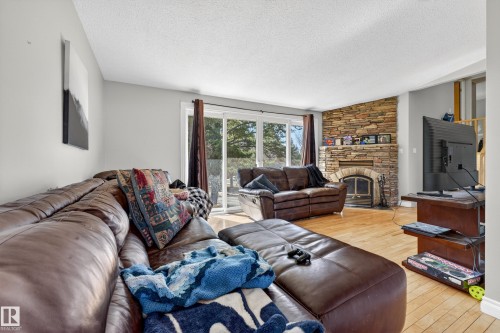 Spacious living area featuring light wood-finish flooring, light grey walls, and a prominent stone-clad fireplace with a hearth and firebox - 1 Greenwich Crescent, St. Albert, AB - Indoor Photo Showing Living Room With Fireplace