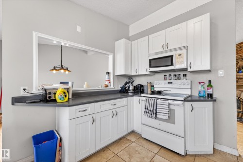 Kitchen featuring white shaker-style cabinetry, dark countertops, and a white range with an above-range microwave - 1 Greenwich Crescent, St. Albert, AB - Indoor Photo Showing Kitchen