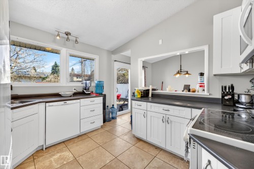Bright kitchen featuring white cabinetry, dark countertops, a built-in dishwasher, and tile flooring - 1 Greenwich Crescent, St. Albert, AB - Indoor Photo Showing Kitchen