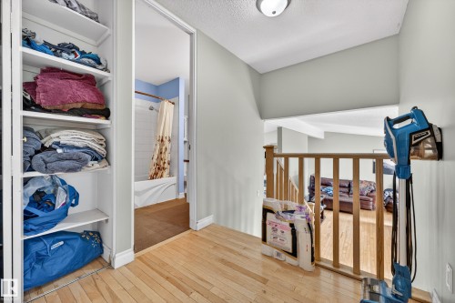 Hallway featuring wood-finish flooring, built-in open shelving, and a wood railing with vertical spindles - 1 Greenwich Crescent, St. Albert, AB - Indoor