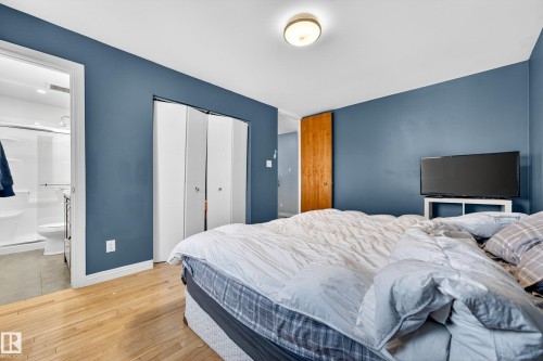 Bedroom featuring wood-finish flooring, a flush-mount ceiling light fixture, a wood panel door, and white bi-fold closet doors - 1 Greenwich Crescent, St. Albert, AB - Indoor Photo Showing Bedroom