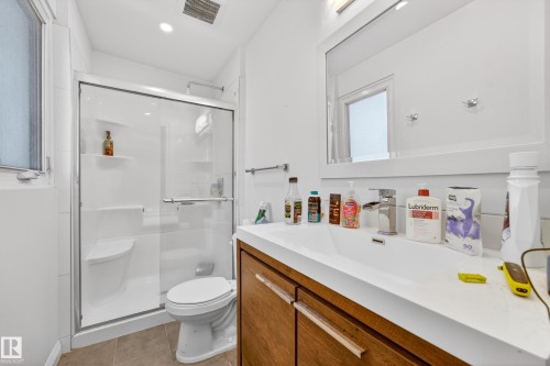 Contemporary bathroom featuring a framed mirror, a single vanity with a white countertop, and a wood-finish cabinet with horizontal hardware - 1 Greenwich Crescent, St. Albert, AB - Indoor Photo Showing Bathroom
