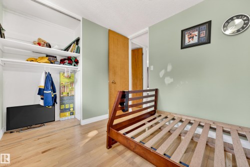 Bedroom with wood-finish flooring, a light green wall, and a built-in closet featuring shelving and a hanging rod - 1 Greenwich Crescent, St. Albert, AB - Indoor