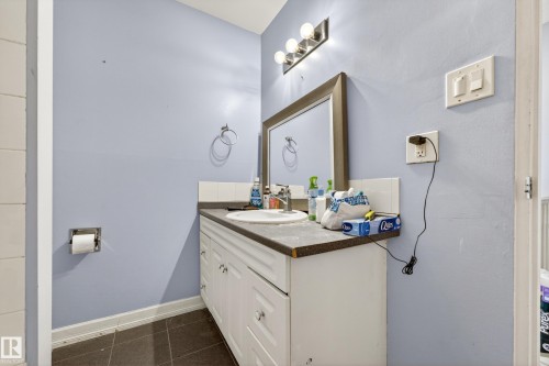 Vanity with a white basin sink and dark countertop, complemented by a large framed mirror and four-bulb light fixture - 1 Greenwich Crescent, St. Albert, AB - Indoor Photo Showing Bathroom