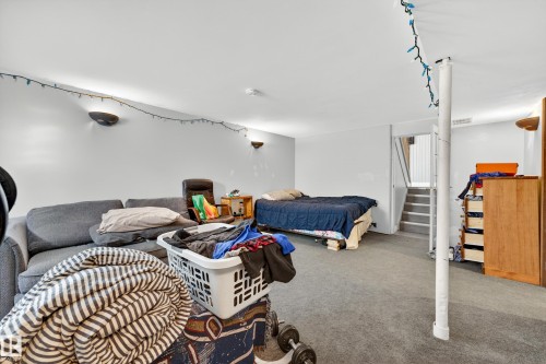 Carpeted room with a support column, wall-mounted sconces, and interior stairs leading to an upper level - 1 Greenwich Crescent, St. Albert, AB - Indoor Photo Showing Bedroom