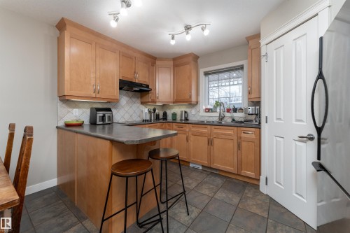 Kitchen featuring freestanding refrigerator, a peninsula, a kitchen bar, backsplash, and dark countertops - 10906 72 Avenue, Edmonton, AB - Indoor Photo Showing Kitchen