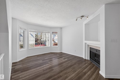 Spacious room featuring wood-finish flooring, a multi-pane window array, and a built-in fireplace with an integrated shelving unit - 6 1237 Carter Crest Road, Edmonton, AB 
