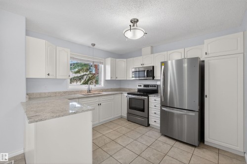 Kitchen featuring white cabinetry, light-toned granite countertops, stainless steel appliances, and ceramic tile flooring - 6 1237 Carter Crest Road, Edmonton, AB 