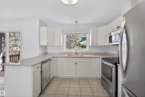 Bright kitchen featuring white cabinetry, light-toned countertops, stainless steel appliances, tile flooring, and a sliding glass door - 6 1237 Carter Crest Road, Edmonton, AB 