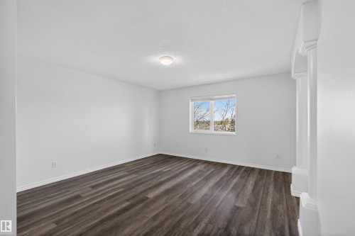 Spacious room featuring wood-finish flooring, white walls, and a single window with outdoor scenery - 6 1237 Carter Crest Road, Edmonton, AB 