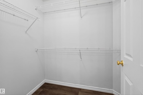 Walk-in closet featuring white wire shelving, wood-finish flooring, and a white paneled door with a brass knob - 6 1237 Carter Crest Road, Edmonton, AB 