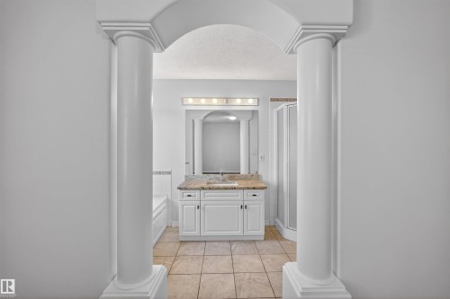 Arched entryway with columns framing a bathroom featuring a white vanity with a light-toned countertop, a frameless mirror, and a multi-bulb vanity light - 6 1237 Carter Crest Road, Edmonton, AB 