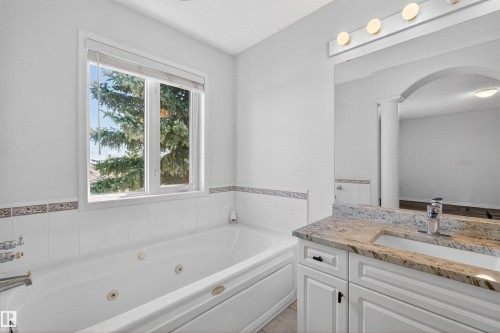 White jetted tub with tiled surround, dual windows, and decorative border tile - 6 1237 Carter Crest Road, Edmonton, AB 