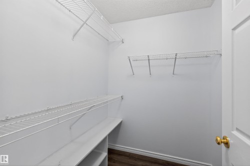 Walk-in closet featuring white wire shelving, built-in lower shelving, wood-finish flooring, and a white paneled door with brass hardware - 6 1237 Carter Crest Road, Edmonton, AB 