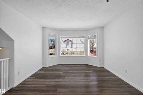 Bright interior room featuring a bay window, wood-finish flooring, white baseboards, a textured ceiling, and a white railing - 6 1237 Carter Crest Road, Edmonton, AB 